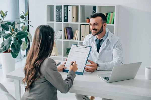 Lächelnder Arzt zeigt Patienten in Klinik Versicherungsantragsformular — Stockfoto