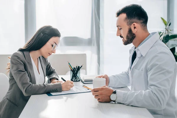 Side view of patient signing insurance claim form in clinic — Stock Photo