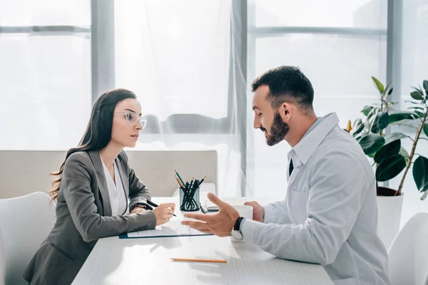 Vista laterale del paziente firma modulo di richiesta di assicurazione in clinica e guardando il medico — Foto stock