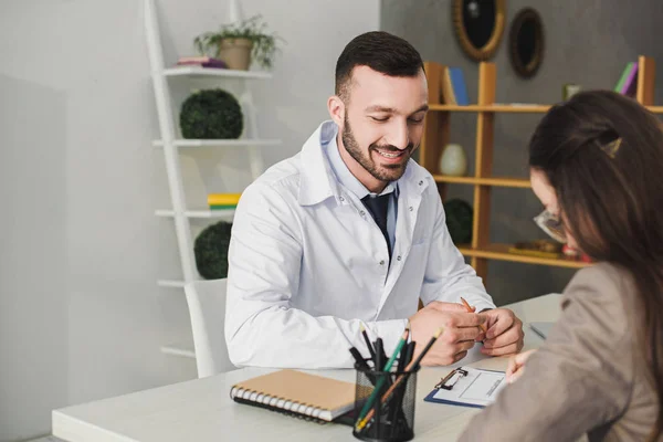 Patient signing insurance claim form in clinic, smiling doctor holding pencil — Stock Photo