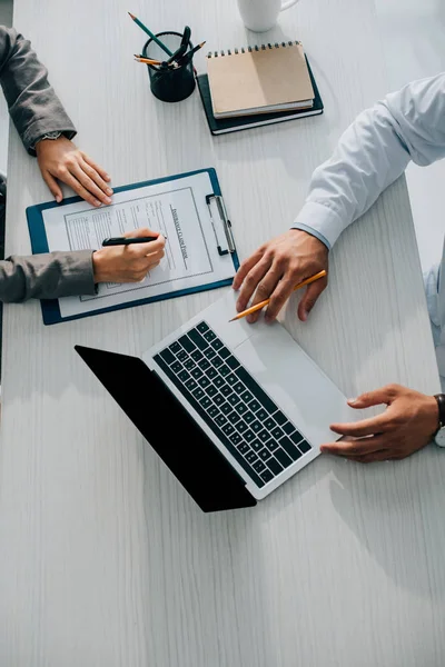 Cropped image of patient signing insurance claim form in clinic, doctor using laptop — Stock Photo