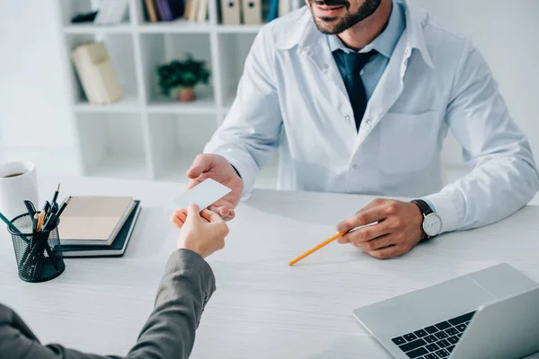 Imagen recortada de paciente dando tarjeta de visita al médico en la clínica - foto de stock