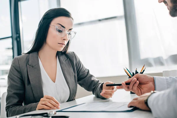 Imagen recortada del médico dando pluma al paciente femenino para firmar el formulario de reclamación de seguro en la clínica - foto de stock