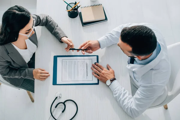 Vista de ángulo alto del médico que da pluma al paciente para firmar el formulario de reclamación de seguro en la clínica - foto de stock