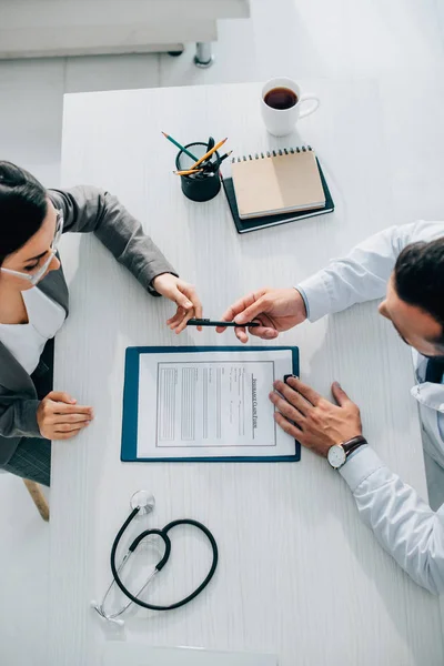 Vue grand angle du médecin donnant stylo au patient pour signer le formulaire de demande de règlement d'assurance dans la clinique — Photo de stock