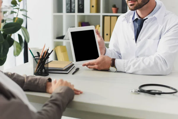 Imagen recortada del médico mostrando tableta con pantalla en blanco al paciente en la clínica - foto de stock