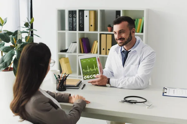Smiling doctor showing patient gadget with pulse appliance in clinic — Stock Photo