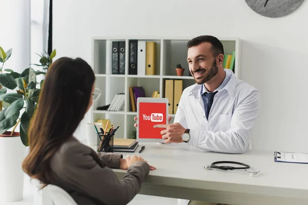 Lächelnder Arzt zeigt auf Tablet mit geladener Youtube-Seite in Klinik — Stockfoto