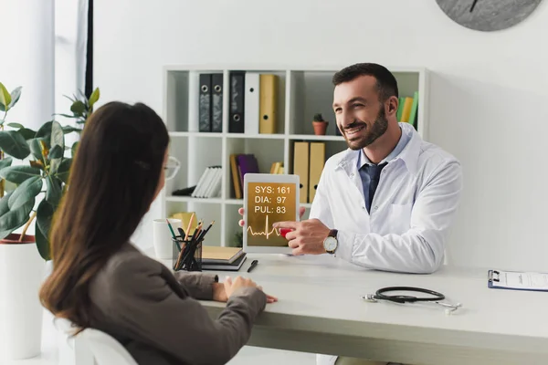 Médico mostrando tablet paciente com aparelho de pulso na clínica — Fotografia de Stock