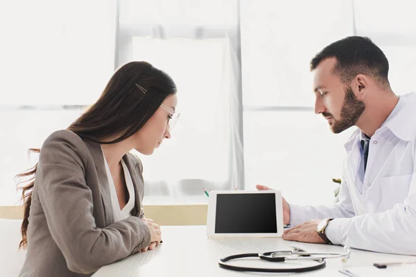 Médecin montrant gadget patient avec écran blanc dans la clinique — Photo de stock