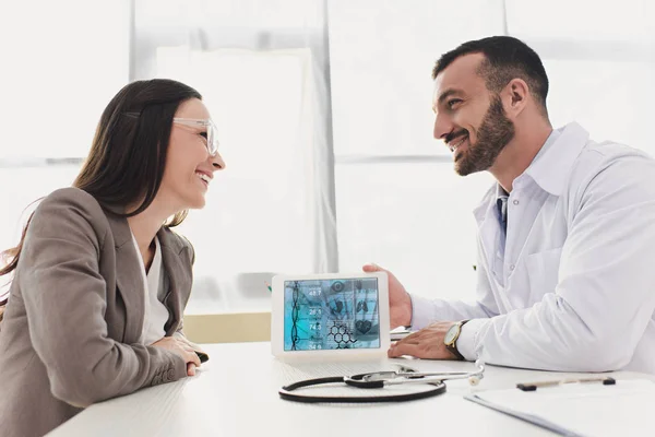 Medico sorridente che mostra tablet paziente con app medica in clinica — Foto stock