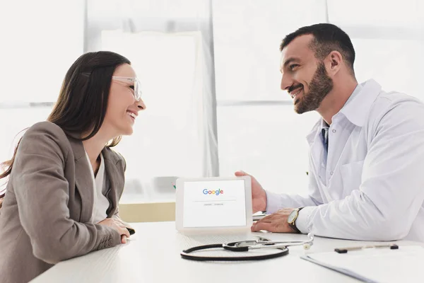Médico sorrindo mostrando tablet paciente com página do google carregado na clínica — Fotografia de Stock
