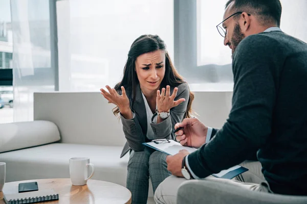 Paciente llorando hablando y psicólogo tomando notas en el consultorio médico - foto de stock