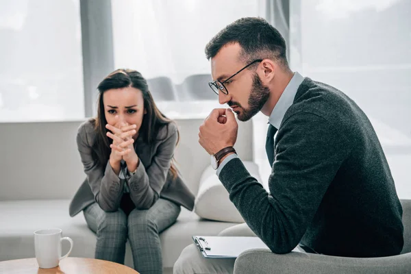 Paciente deprimido llorando y psicólogo pensativo sentado en el consultorio médico - foto de stock