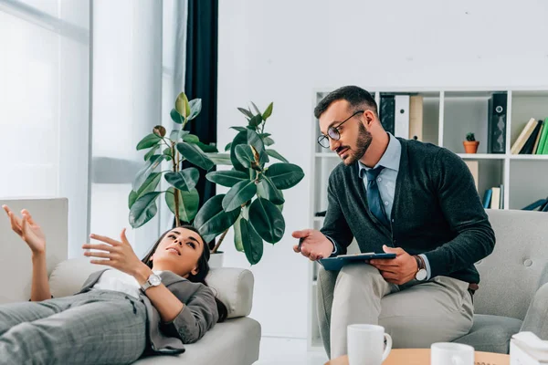 Patient couché sur le canapé et parlant au thérapeute au bureau — Photo de stock