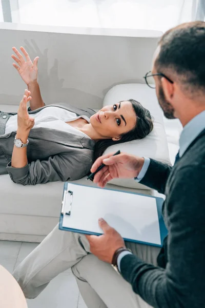 High angle view of patient lying on sofa and talking with psychologist in office — Stock Photo