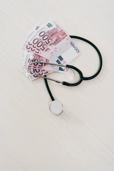 Vista elevada del estetoscopio y los billetes en euros sobre la mesa en la clínica, concepto de seguro de salud - foto de stock