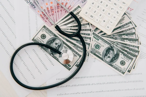 Erhöhter Blick auf Stethoskop, Geld und Taschenrechner auf dem Tisch in der Klinik, Krankenkassenkonzept — Stockfoto