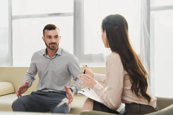 Paciente masculino y psicólogo profesional con portapapeles en el consultorio - foto de stock