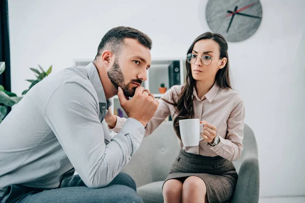 Professional psychologist giving cup of tea to thoughtful patient in office — Stock Photo