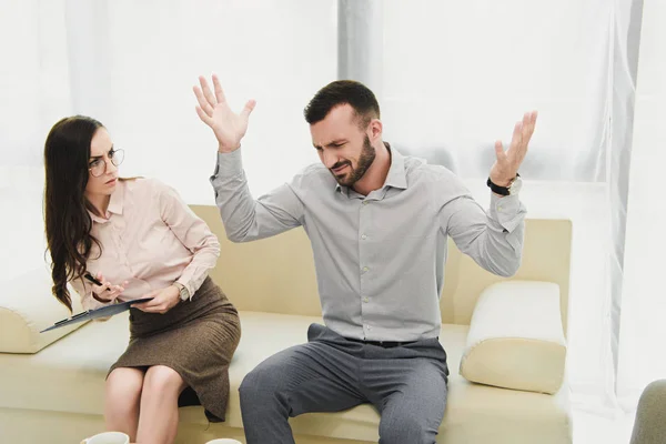 Female psychiatrist with clipboard listening emotional patient gesturing in office — Stock Photo