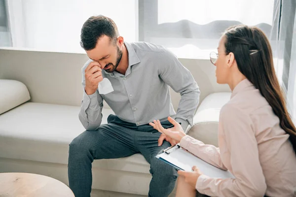 Психолог з буфетом розмовляє з плачучим пацієнтом чоловічої статі в офісі — стокове фото