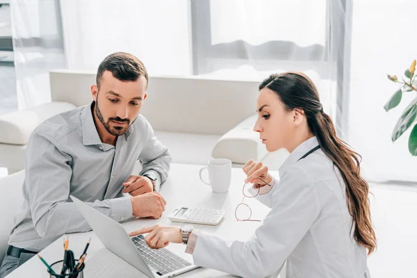 Doctora mostrando algo en el portátil al cliente en la oficina - foto de stock