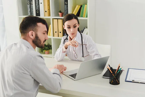Female doctor and client discussing life insurance and looking on laptop screen in medical office — Stock Photo
