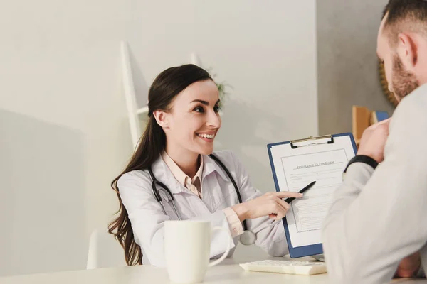 Lächelnder Arzt zeigt Klient in Klinik Versicherungsantragsformular — Stockfoto