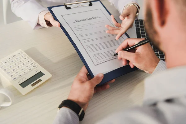 Vista ritagliata del cliente firma modulo di richiesta di assicurazione in studio medico — Foto stock