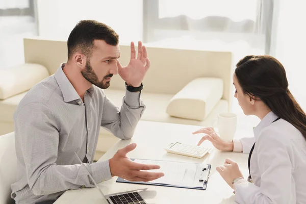 Cliente frustrado mirando al médico contando las finanzas en la calculadora, concepto de seguro de vida - foto de stock