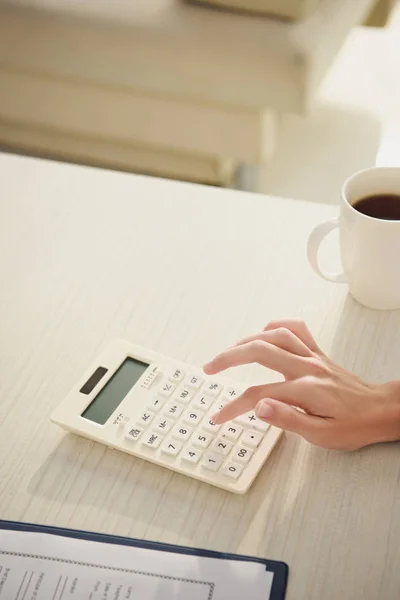 Cropped view of woman counting finances on calculator at table with cup of coffee — Stock Photo