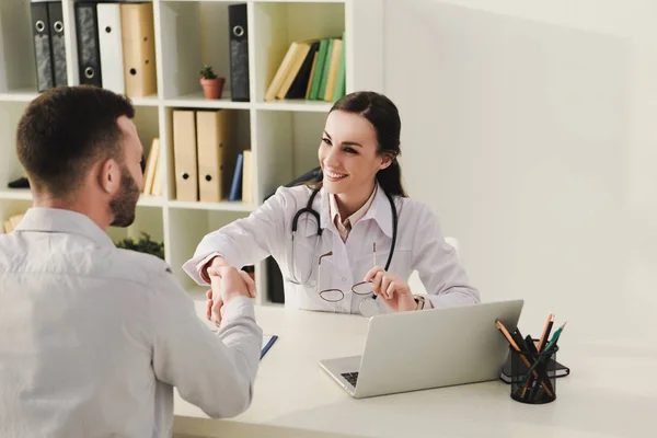 Cliente y médico sonriente estrechando las manos en el consultorio médico - foto de stock