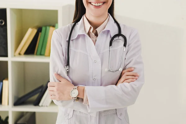 Обрезанный вид улыбающегося доктора в белом халате со скрещенными руками — стоковое фото