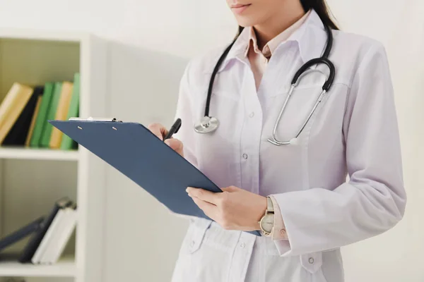 Cropped view of female doctor writing diagnosis in clipboard — Stock Photo