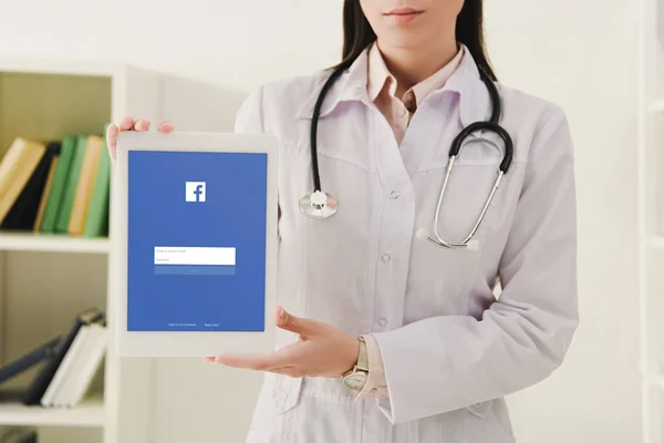 Cropped view of doctor with stethoscope showing digital tablet with facebook app — Stock Photo