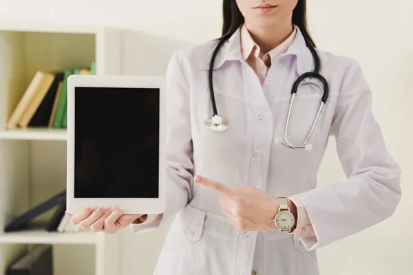 Обрезанный вид врача со стетоскопом, указывающий на цифровой планшет с пустым экраном — стоковое фото
