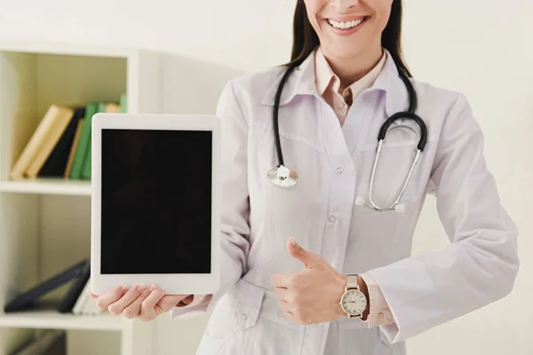 Vista recortada del médico mostrando el pulgar hacia arriba y la presentación de la tableta digital con pantalla en blanco - foto de stock