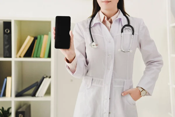 Cropped view of female doctor presenting smartphone with blank screen — Stock Photo