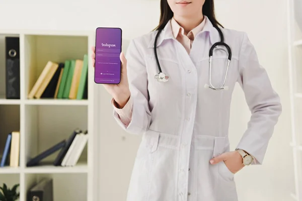 Cropped view of doctor with stethoscope showing smartphone with instagram app — Stock Photo