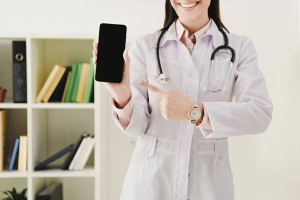Vue recadrée du médecin pointant vers le smartphone avec écran blanc — Photo de stock