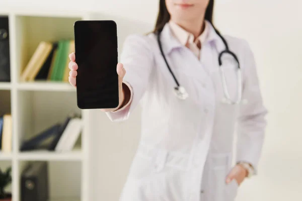 Cropped view of doctor showing smartphone with blank screen — Stock Photo