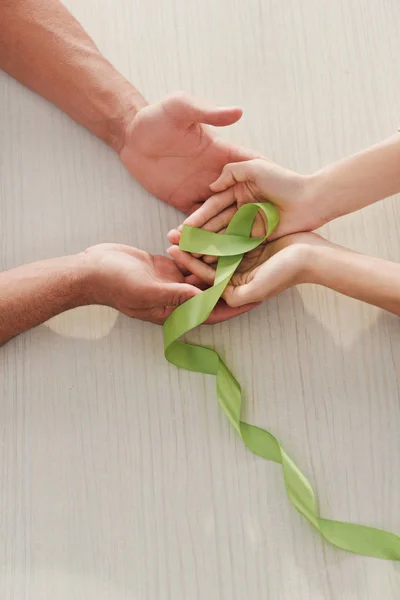 Cropped view of male and female hands holding green ribbon - mental health day — Stock Photo