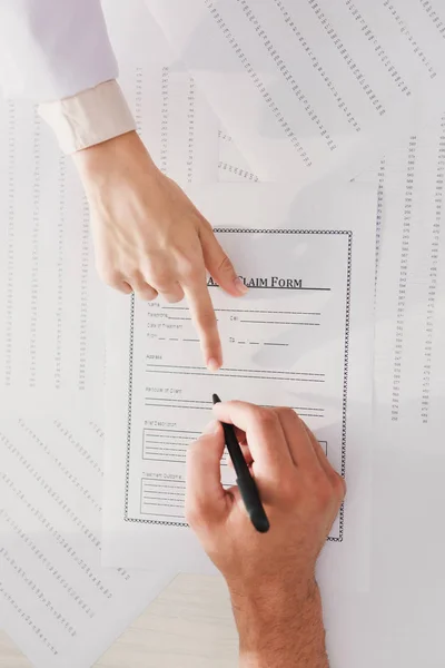 Top view of man signing insurance claim form while doctor pointing at it — Stock Photo