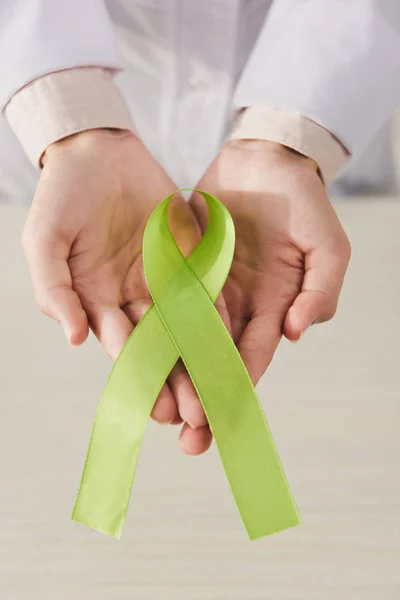 Vue partielle du médecin tenant un ruban vert dans les mains - journée de la santé mentale — Photo de stock