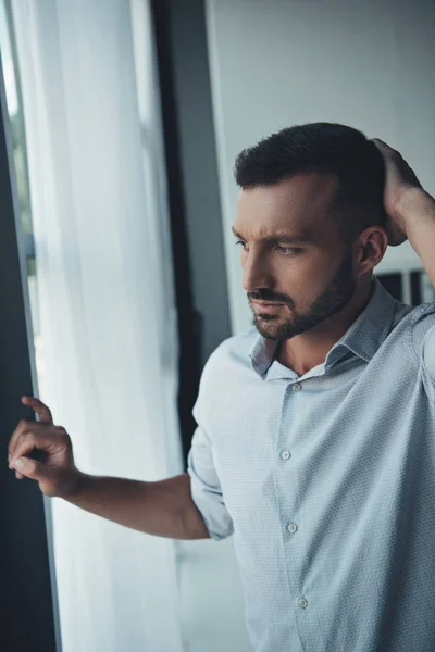 Thoughtful lonely man standing at window at home — Stock Photo