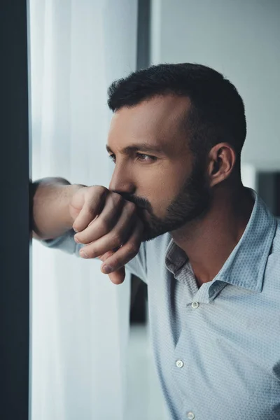 Thoughtful man standing at window at home — Stock Photo