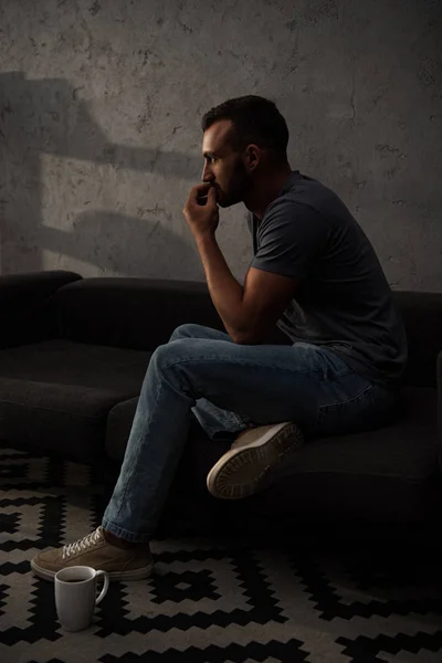 Вдумливий чоловік сидить на дивані з чашкою кави на підлозі — стокове фото