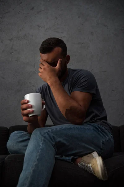 Deprimido llorando hombre sosteniendo taza de café sentado en casa - foto de stock