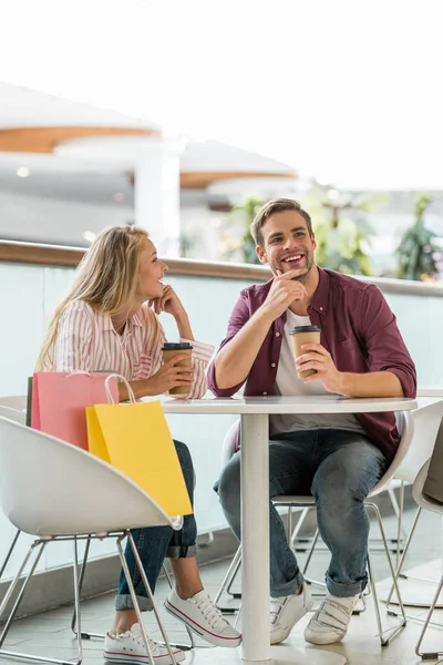 Feliz pareja joven con los insectos de compras en la mesa con tazas de café desechables en la cafetería - foto de stock